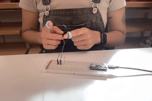 breadboard with arduino powering a blue LED with a jumper wires connected to finger sleeves as a switch